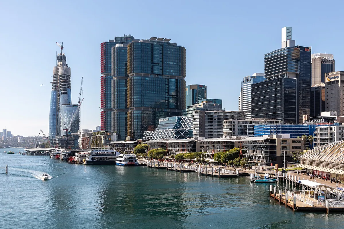 El paseo marítimo de Darling Harbour de día, con barcos de crucero amarrados a lo largo de los muelles frente a las torres de la ciudad y un embarcadero de ferris a la derecha.